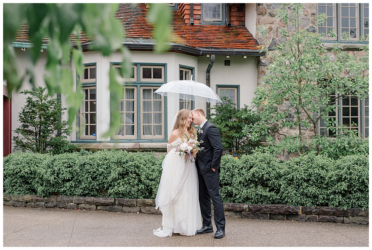 Groom kisses bride under a clear umbrella during a rainy wedding day in Columbus, Ohio at Beverly Mansion photographed by Ohio Wedding Photographer