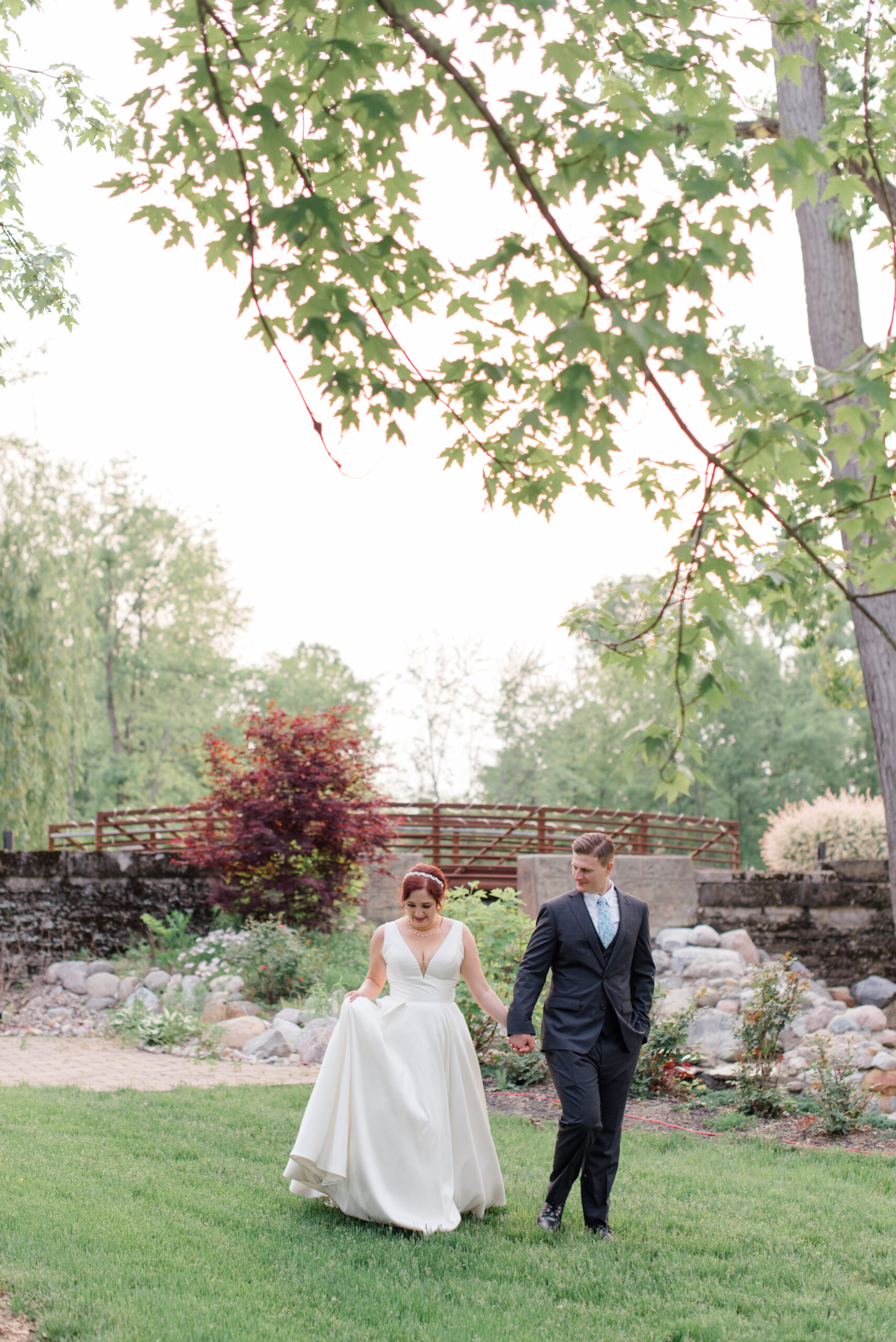 bride adn groom holding hands and walk across a manicured lawn at Swan Lake in the gardens at sunset