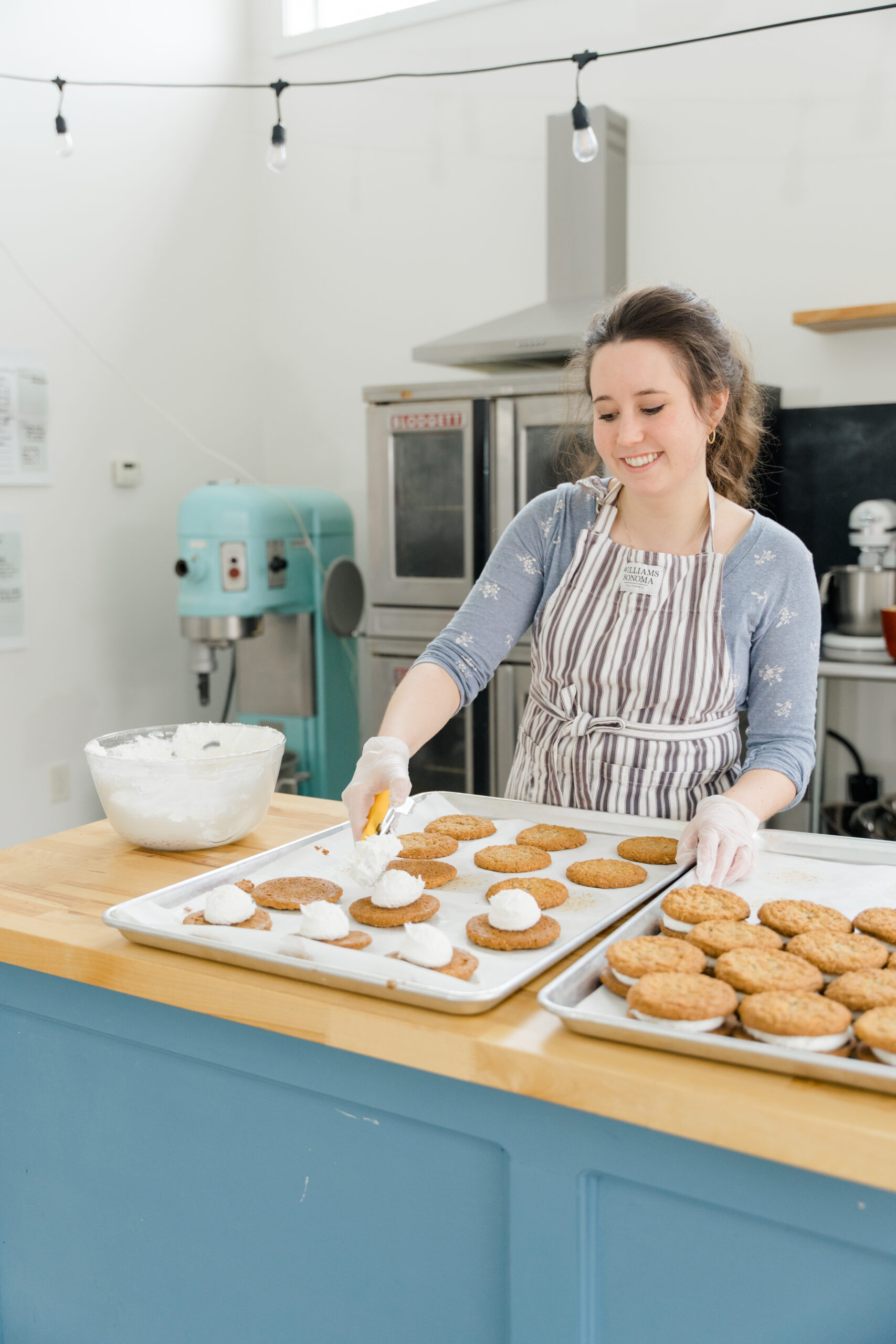woman in a striped apron frosting cookies in a kitchen of a bakery