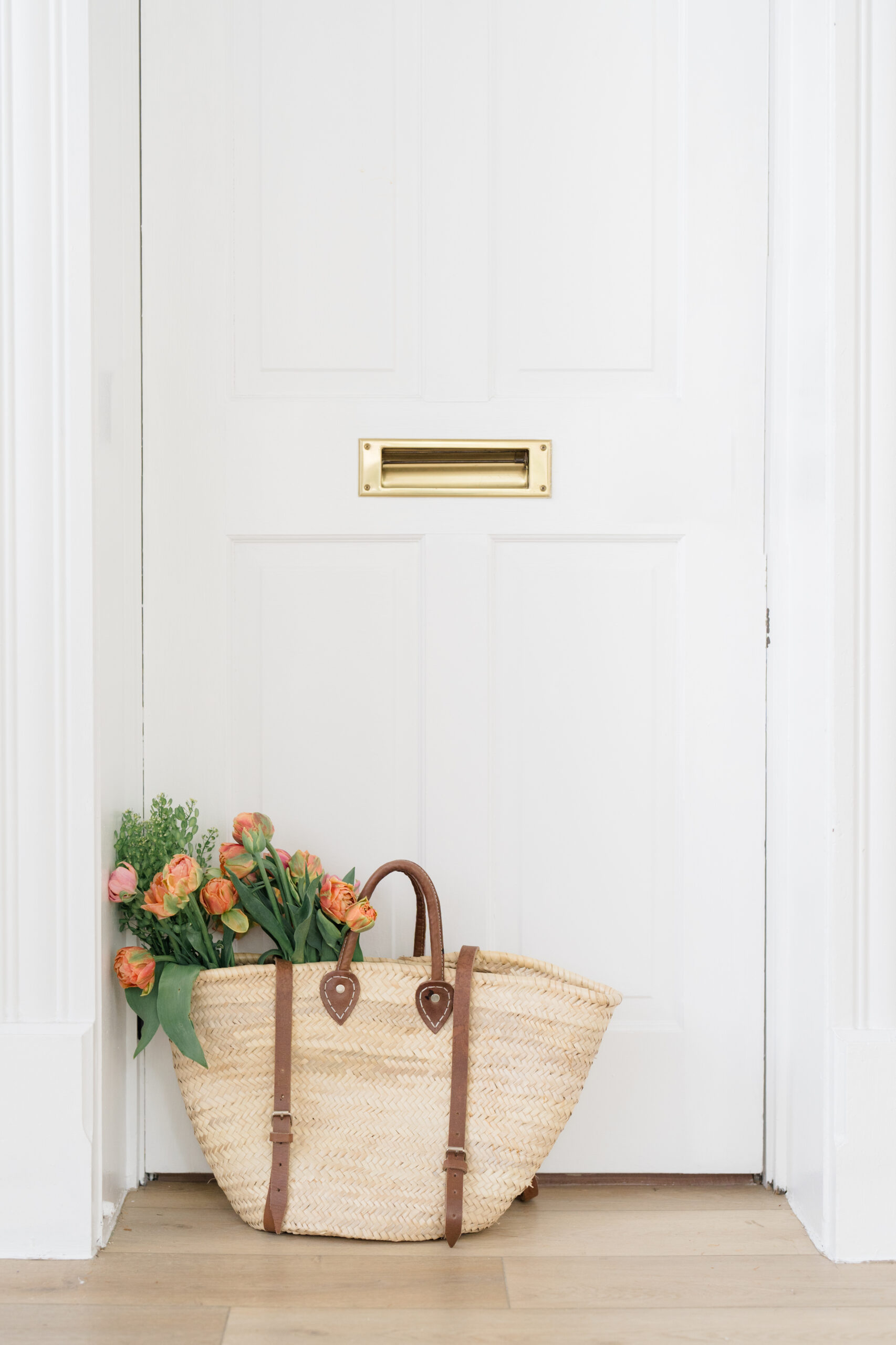 brand photographer in Columbus Ohio with a wicker bag in front of a white door with flowers in the bag