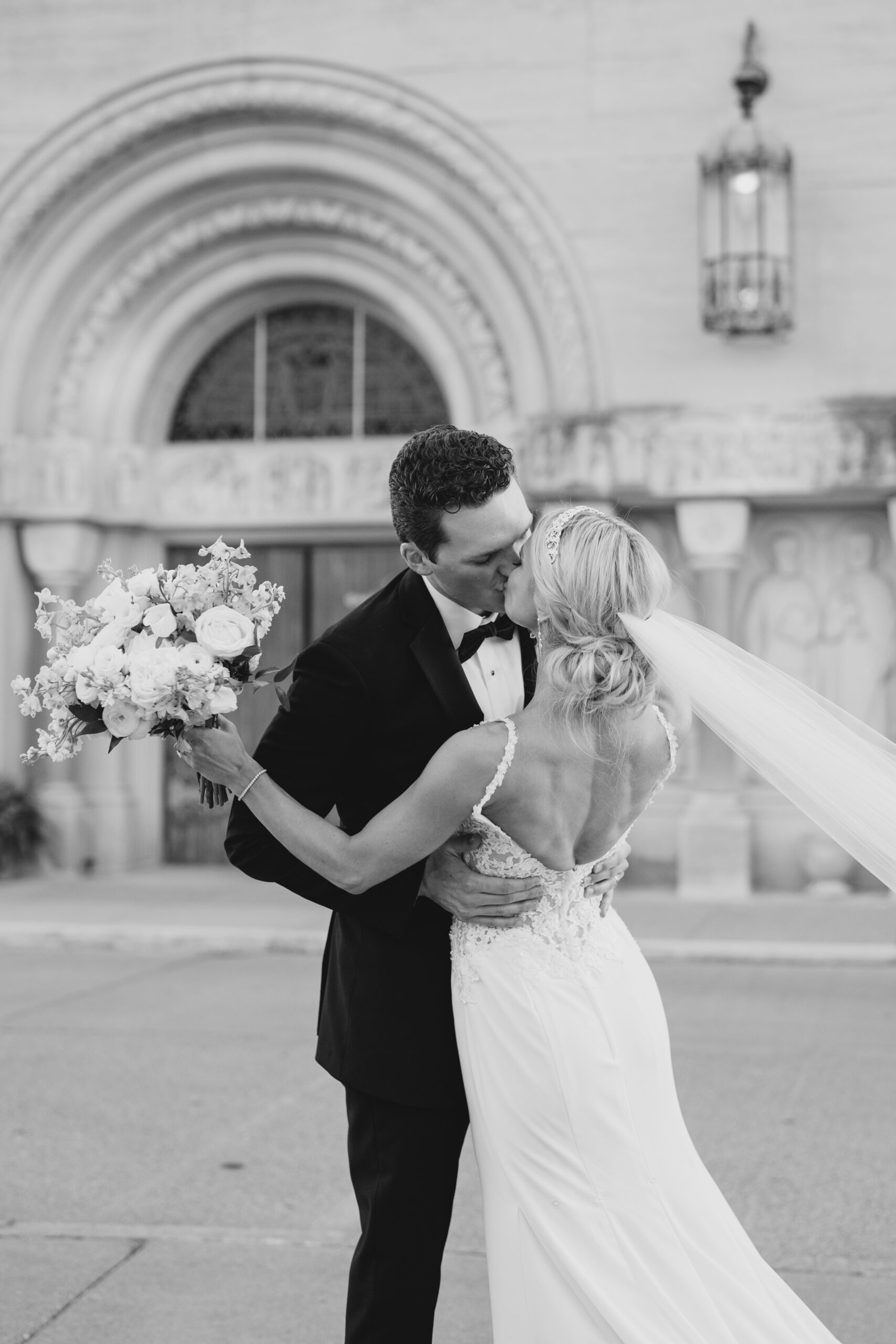 black and white wedding photo of groom kissing his bride as she holds her flower bouquet to the side captured by Ohio photographer