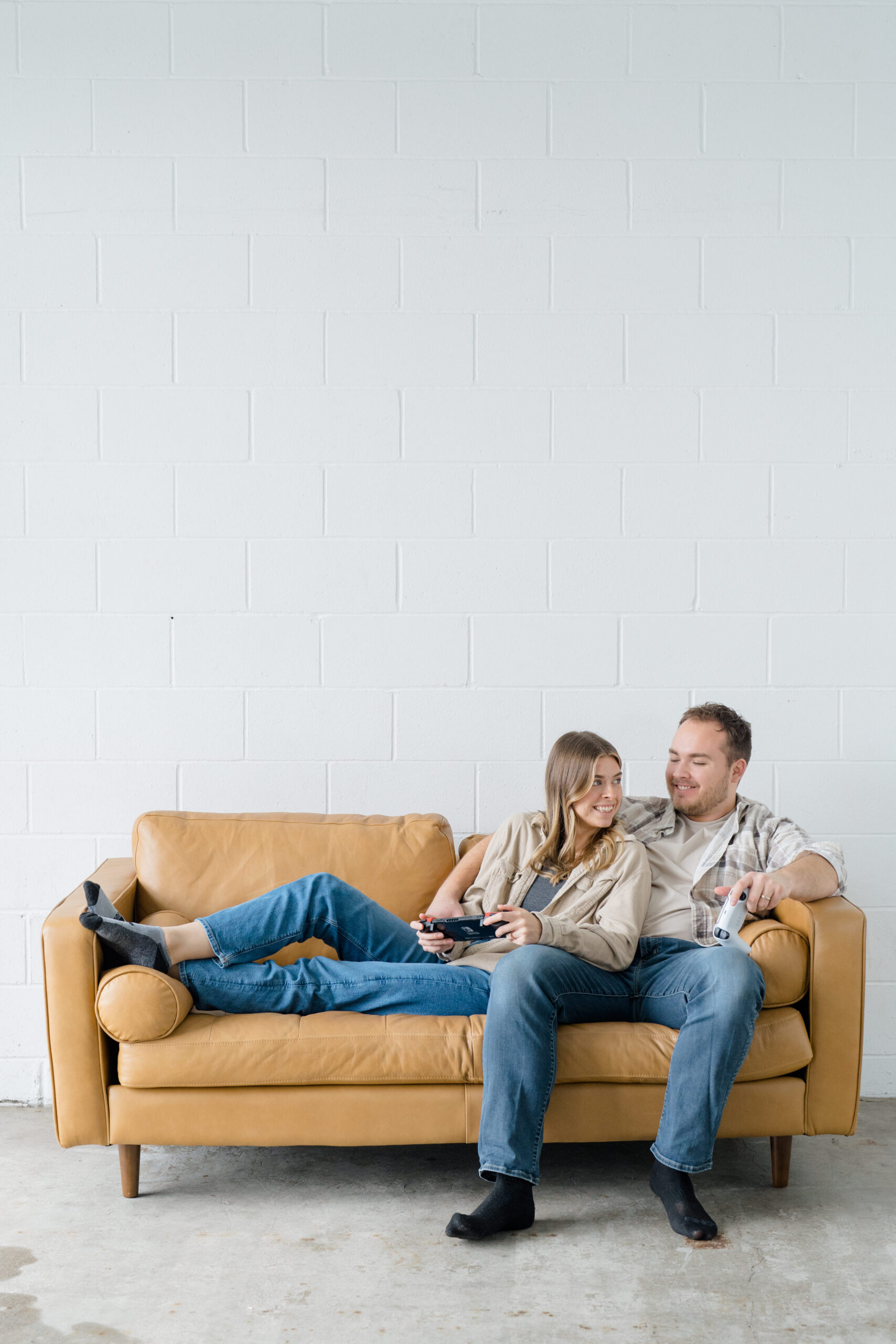 Columbus photographer captures husband and wife team sitting on a couch together with a white backdrop as they relax for candid branding photos