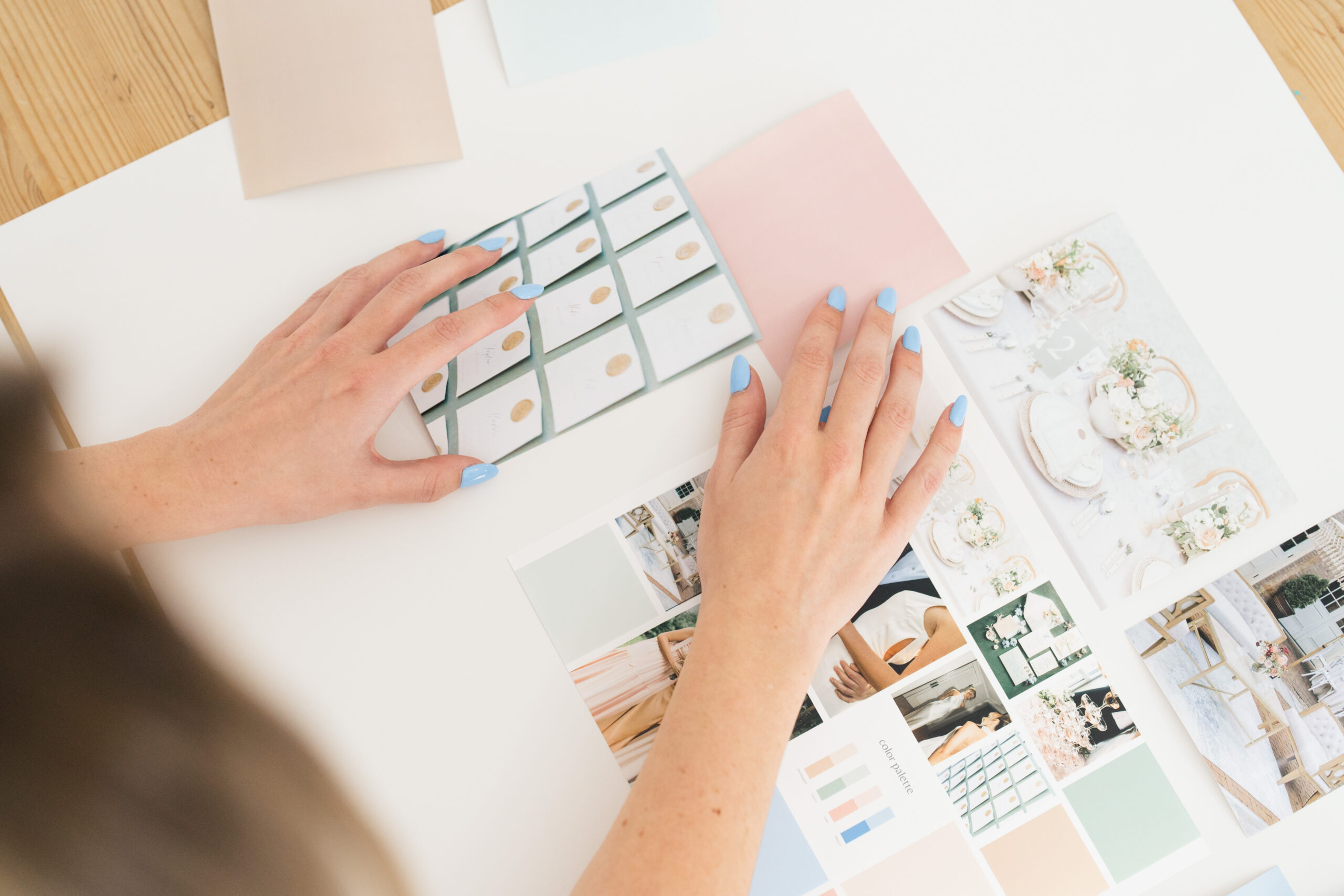 A Columbus photographer captures a brand photo of a woman's hands arranging a wedding inspiration mood board. The board features elegant invitation designs, floral table settings, and a pastel color palette, highlighting creative planning and design aesthetics.