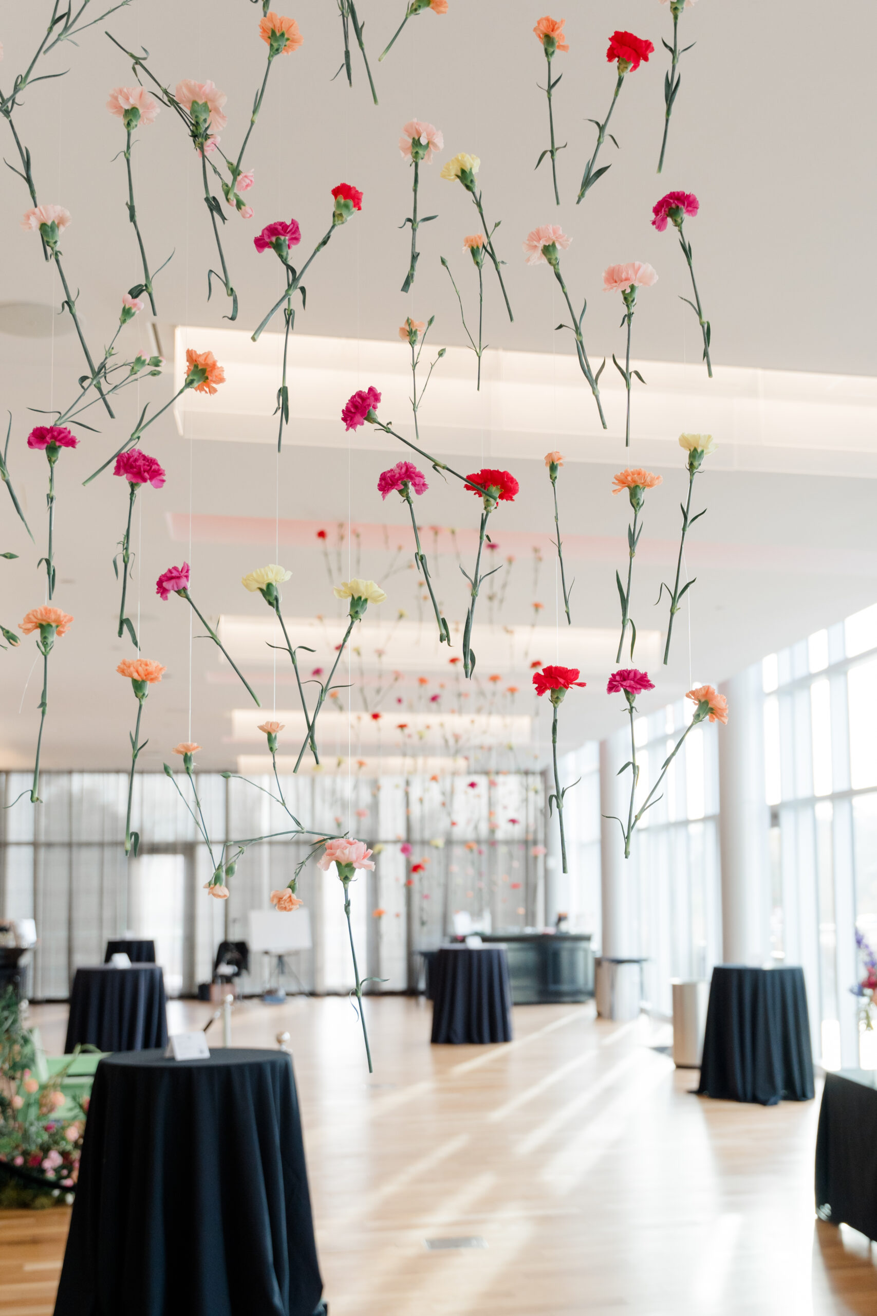 An airy event space featuring hanging arrangements of colorful carnations, black cocktail tables, and a modern bar area, captured as brand photography by a Columbus photographer.