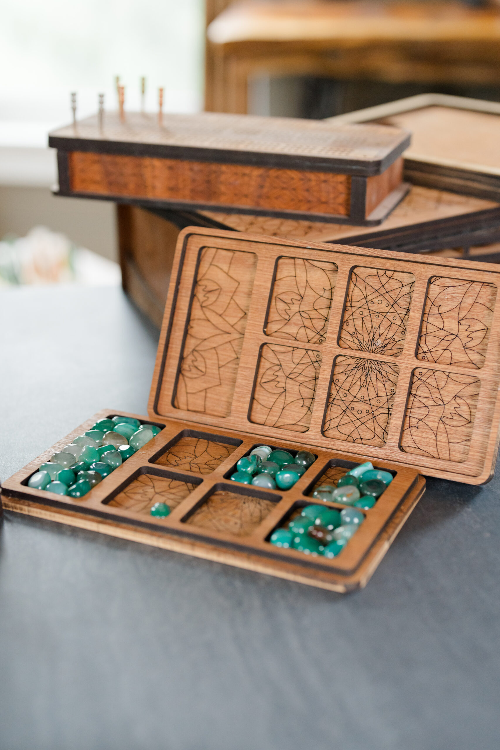 A handcrafted wooden mancala board featuring engraved geometric designs and compartments filled with green and blue playing stones, captured as product photography by a Columbus brand photographer.